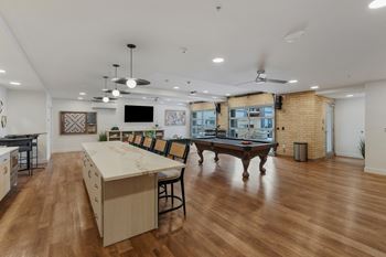 A room with a long table and chairs, a pool table, and a television.